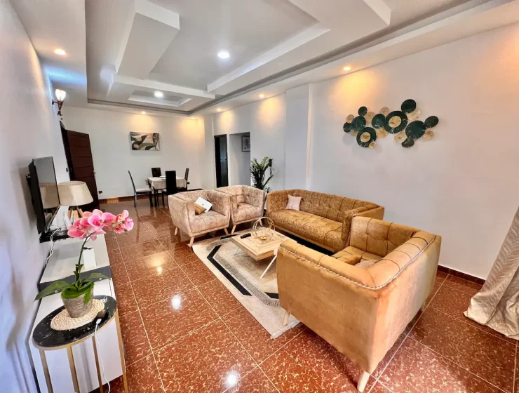 Salon spacieux au design contemporain avec une décoration murale artistique inspirée de la Côte d'Ivoire, un ensemble de canapés en cuir marron, une élégante table basse blanche et un sol en marbre brillant.