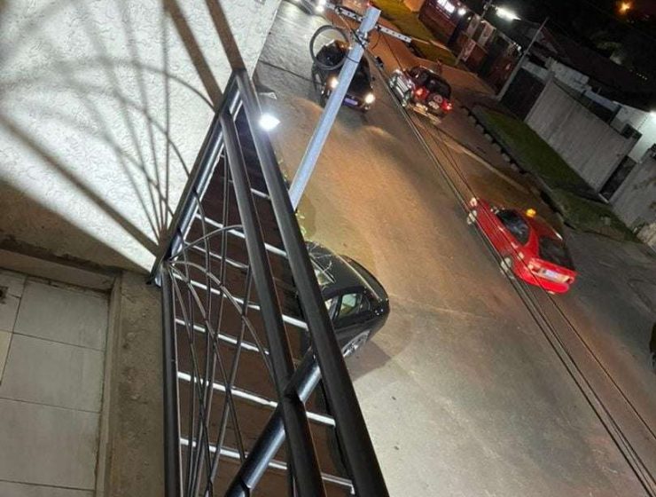Une rue urbaine faiblement éclairée en Côte d'Ivoire la nuit, vue depuis un balcon surélevé avec des balustrades métalliques, avec des voitures garées et passant.