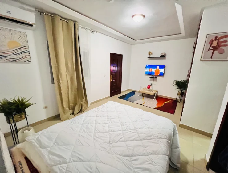Chambre cosy et moderne inspirée de la Côte d'Ivoire avec un grand lit, un éclairage d'ambiance, une télévision au mur et une décoration de bon goût.